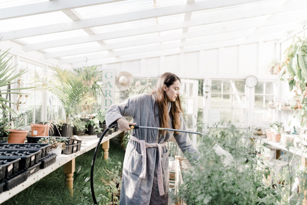 a woman watering plants in a robe in a greenhouse