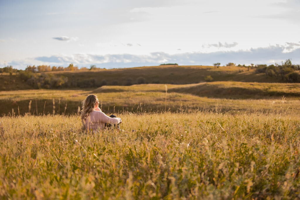 A woman sitting in a field at sunset