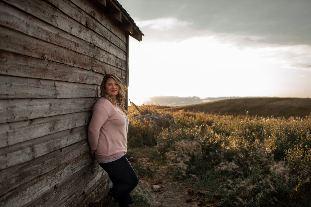 A women standing at the side of a barn at sunset