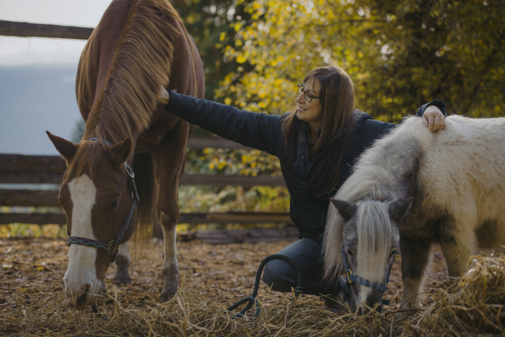 A woman crouching between a quarter horse and a pony