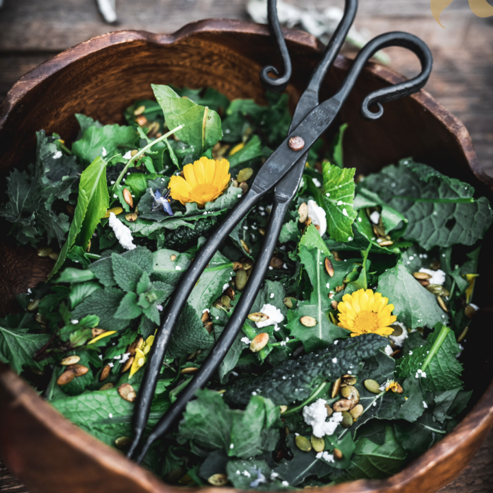 spring salad with greens and spring flowers in a wooden bowl