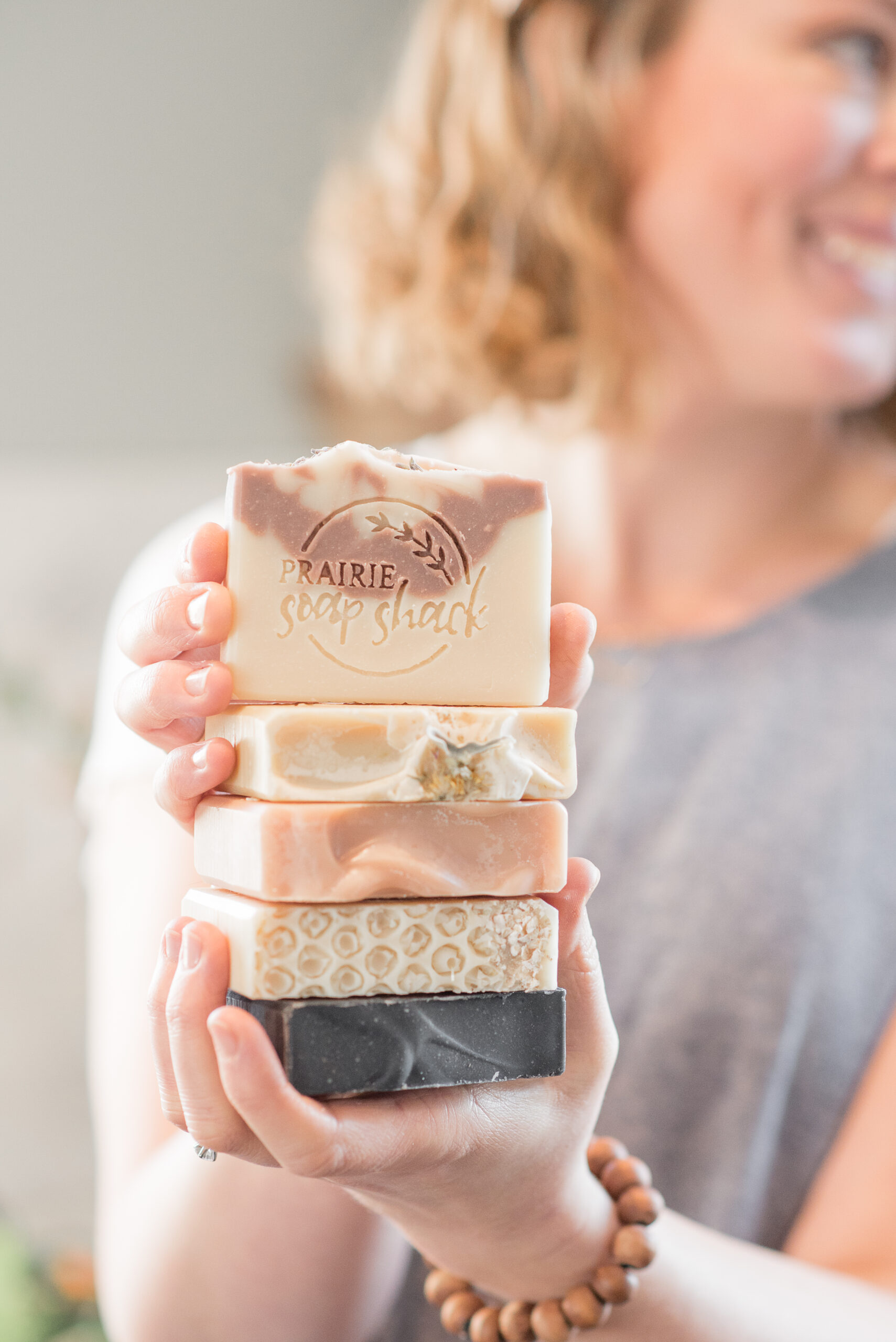 a woman holding a stack of homemade soaps
