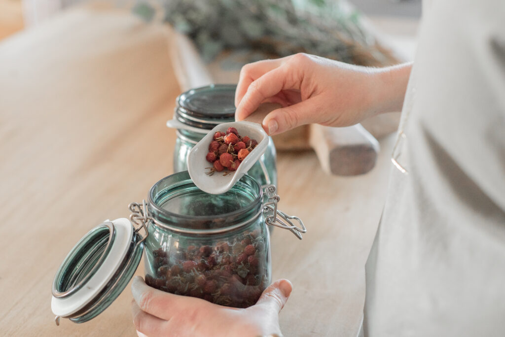 a person pouring dried berries into a mason jar.