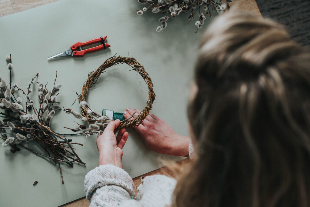 A women wrapping pussy willows onto a wreath form using floral wire.