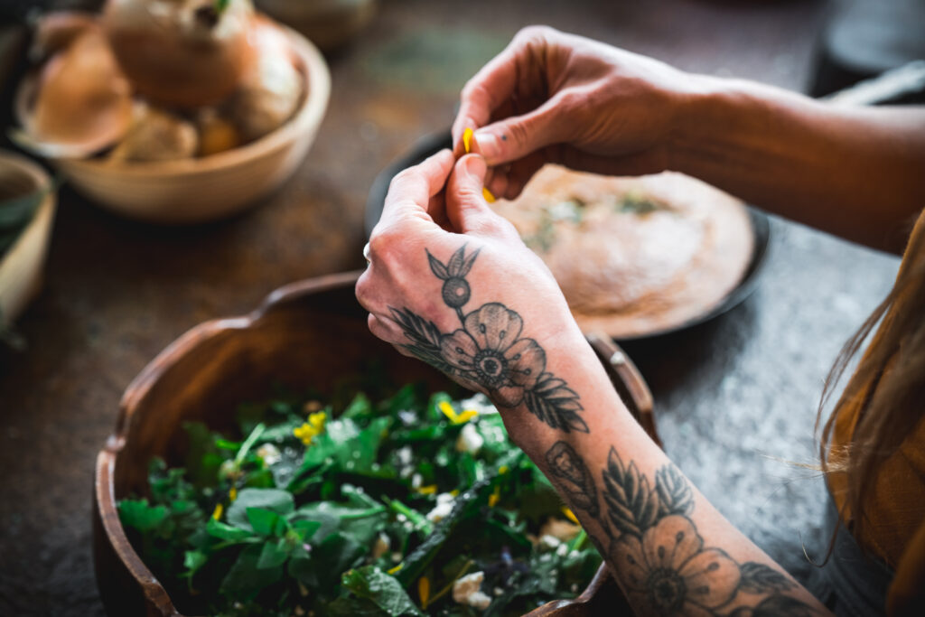 hands with tattoos making a spring salad with fresh edible flowers and garden greens
