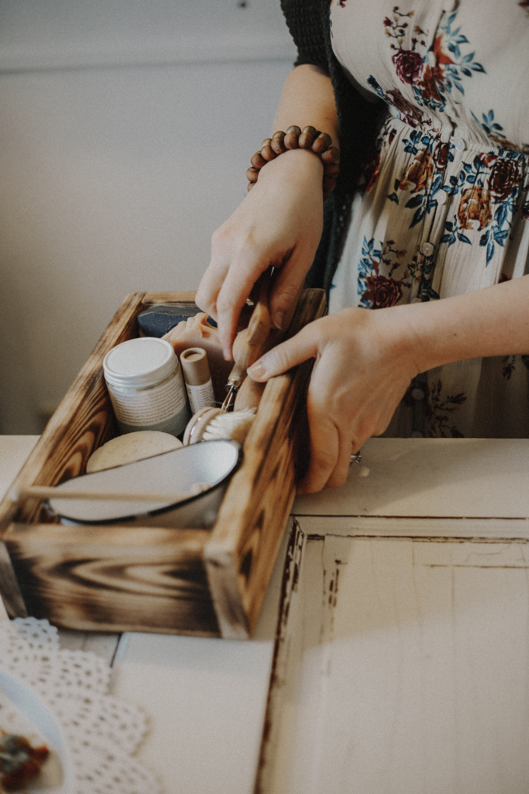 A person's hands organizing skincare products in a wooden caddy on a white table.