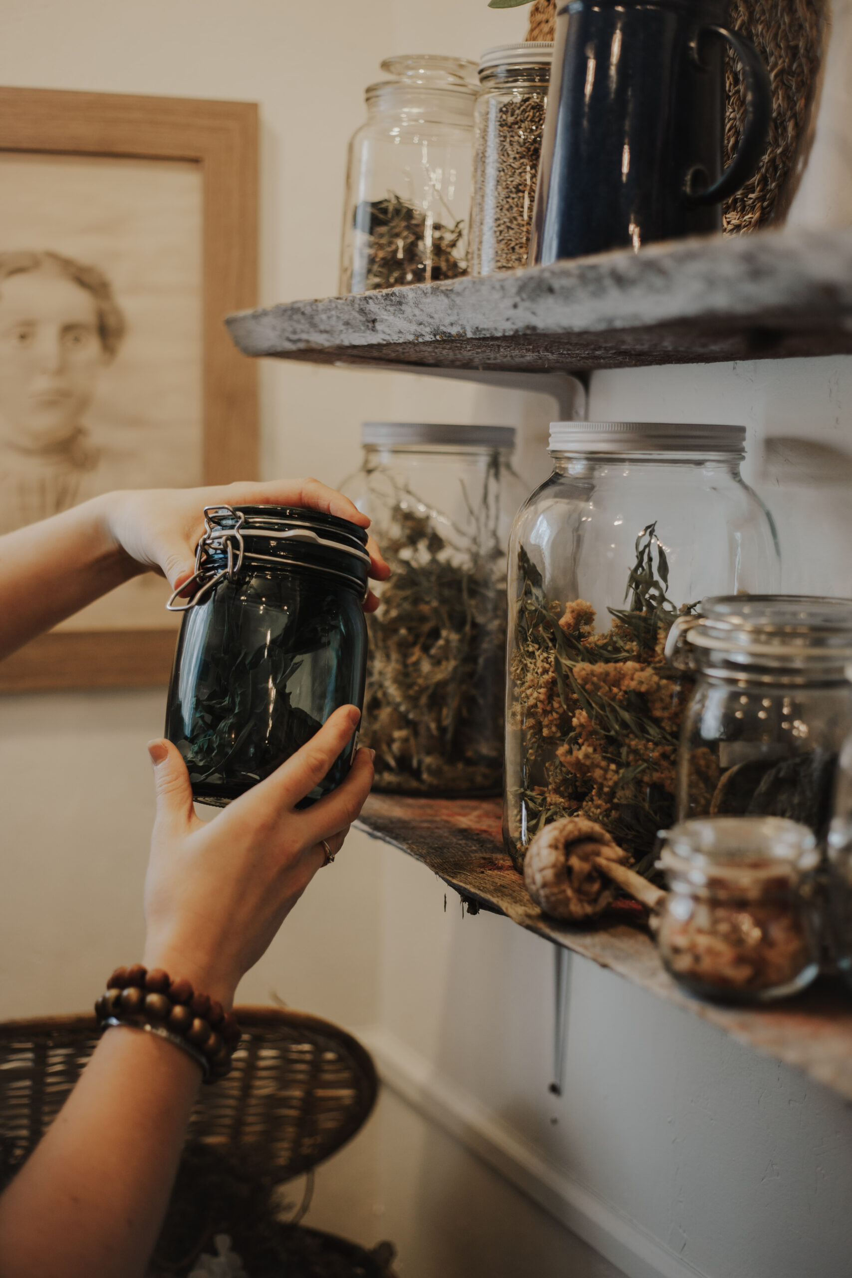 Close-up of a person's hands placing a jar of dried herbs on a rustic shelf beside other jars.