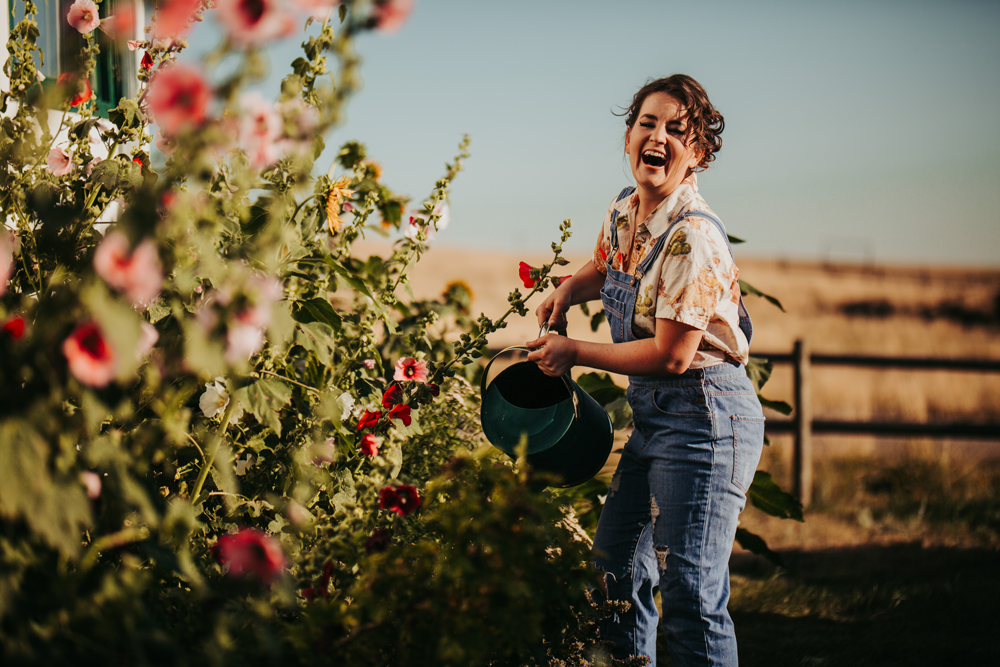 woman laughing while holding a watering can, watering pink flowers