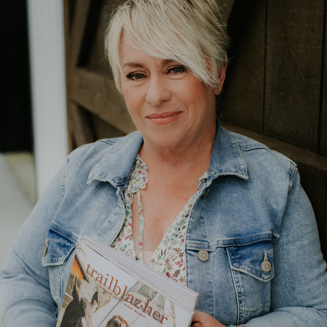 woman with short blonde hair in a blue jean jacket holds a trailblazher magazine