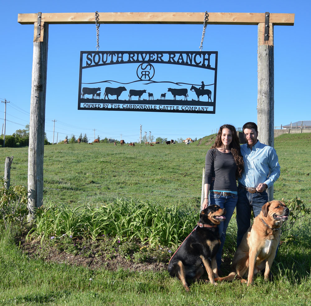 Woman and Man stand with their 2 dogs at their farm sign