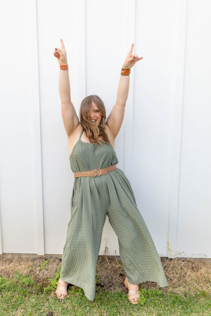 woman in green jumpsuit raising her arms and smiling