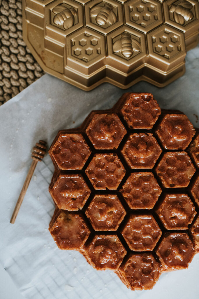 a honeycomb cake sitting on a white tablecloth with a honey stick and a gold honeycomb cake pan