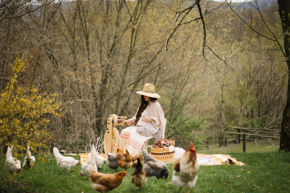 Woman using a spinner outside surrounded by trees, grass and chickens