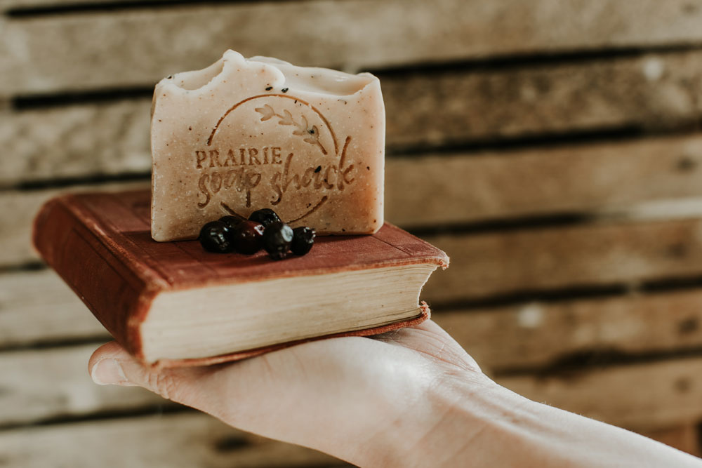 A hand holds a small book with saskatoons on it with a piece of prairie soap shack soap