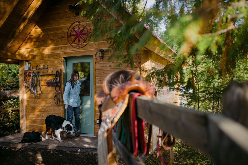 Woman in front of wood cabin with light blue door holding the leash to her black and white dog