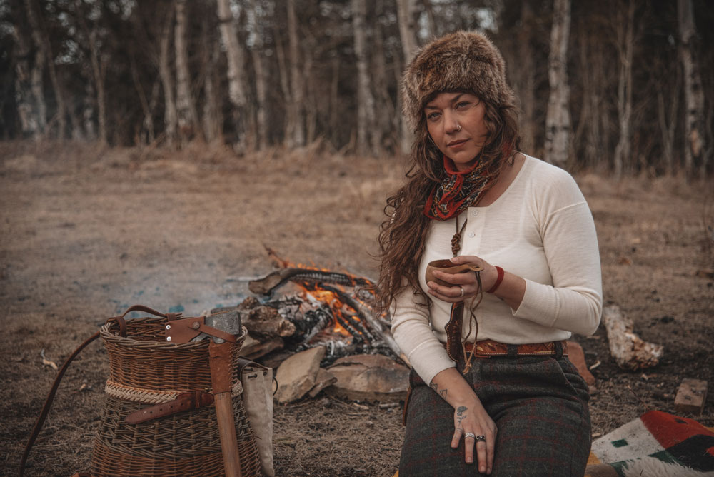 Alyse sits in front of a campfire, holding a mug