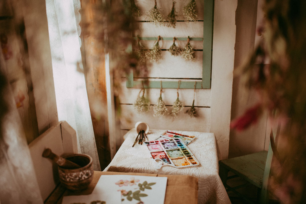 flowers drying on the back wall with a table with watercolour paints in front