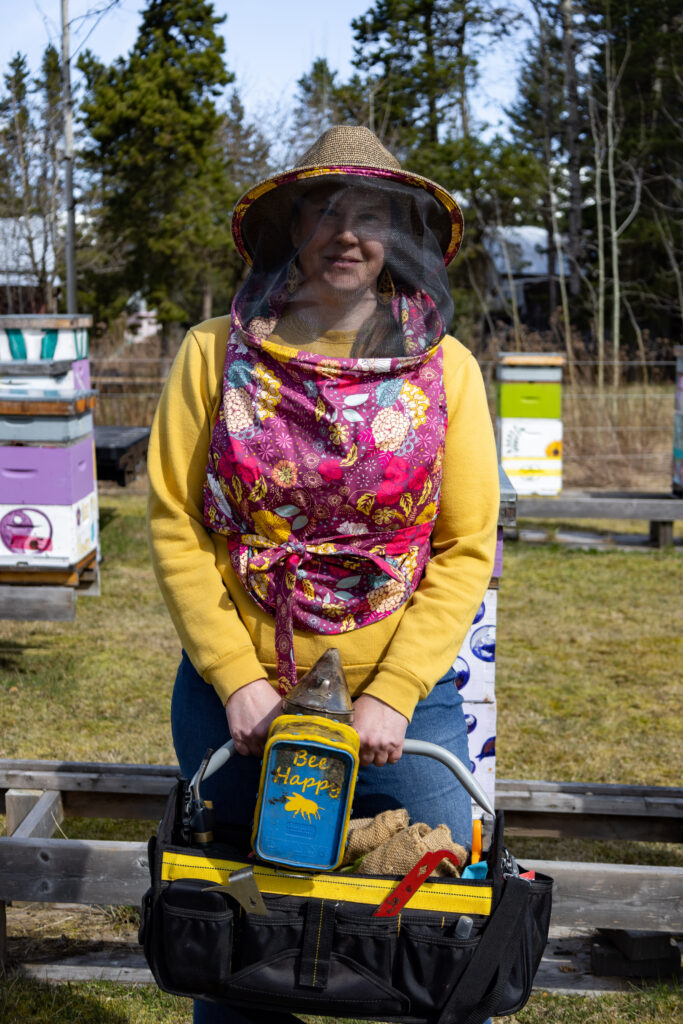 Christine stands around her bee houses in a bee protection hat