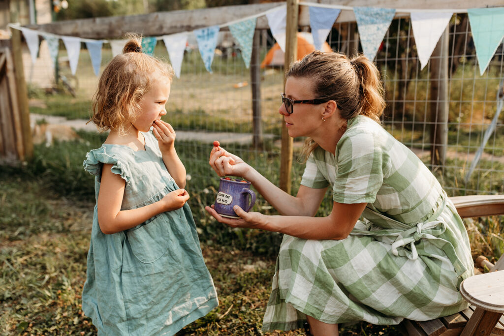 Kate kneels with her daughter and offers her a berry