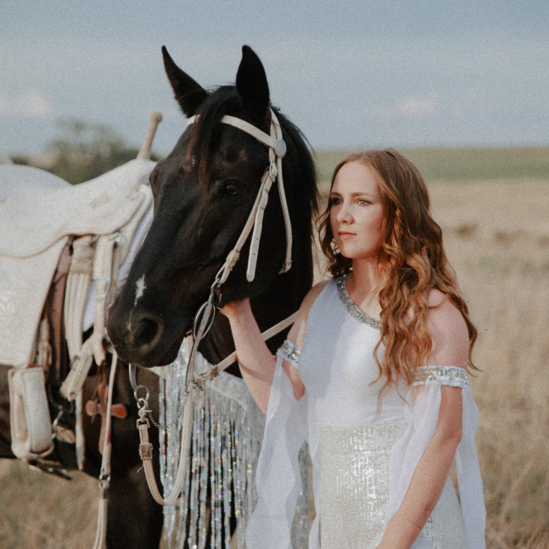 Shelby wears a white dress standing with her dark horse