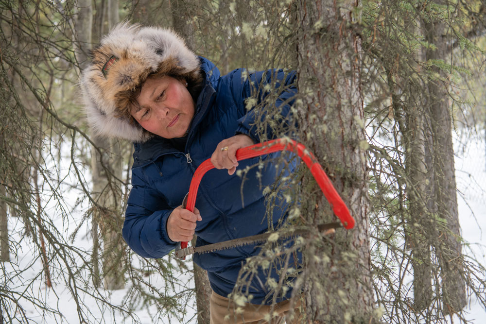 Minnie uses a hand saw on a tree brand outside