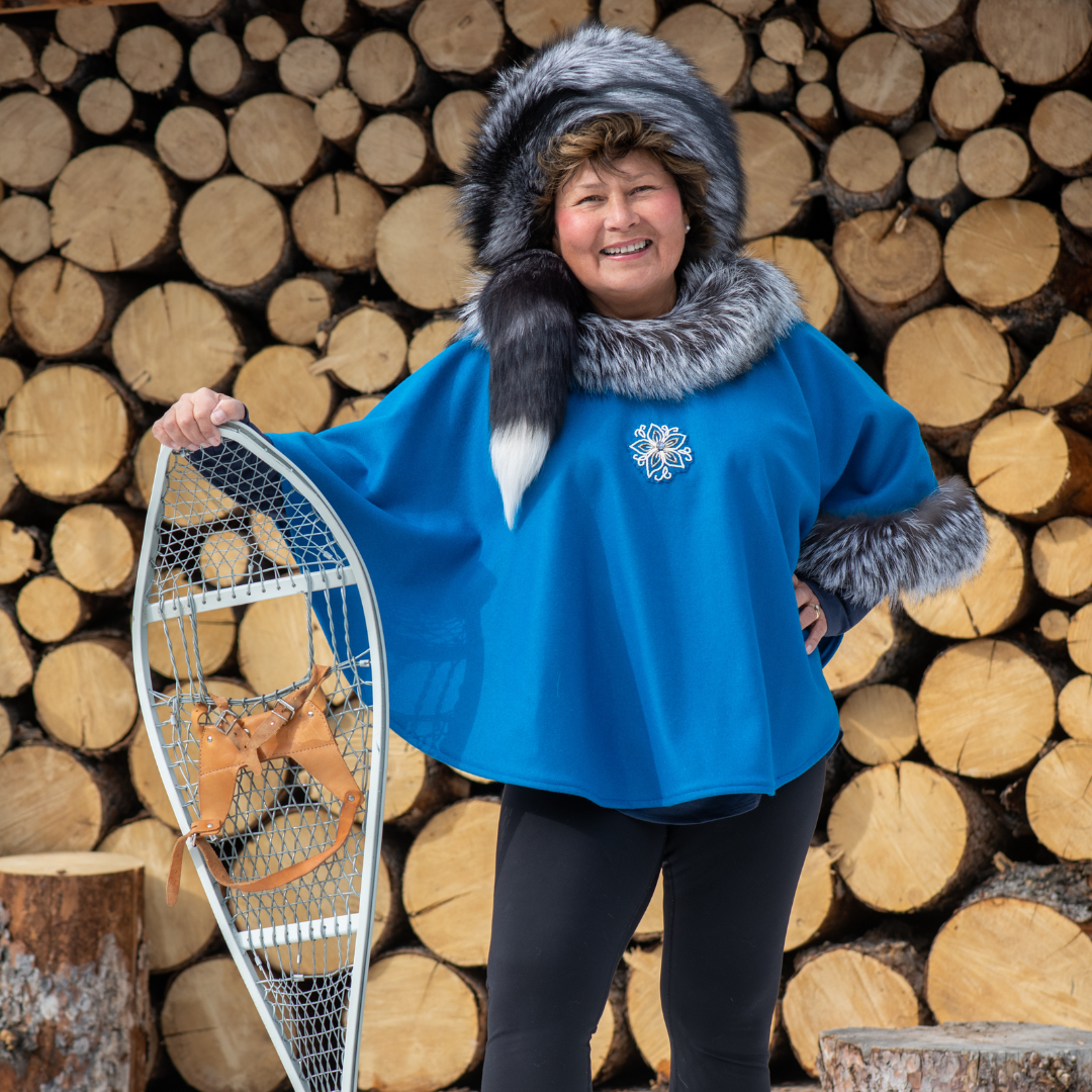 Minnie is wearing a blue poncho style coat standing in front of a pile of logs